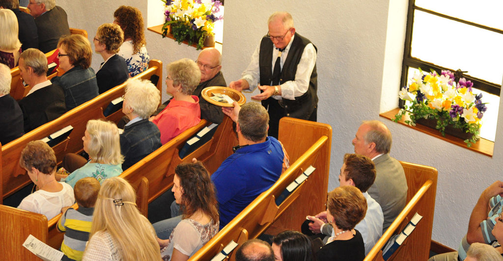 Paul Moses (center), a member of First Baptist Church of Boise City, Okla., collects members’ offering during a Centennial celebration of the church in Summer 2016. The church makes giving to the Lottie Moon Christmas Offering for International Missions a priority every year. (Photo by Holli Bade. Used with permission.)