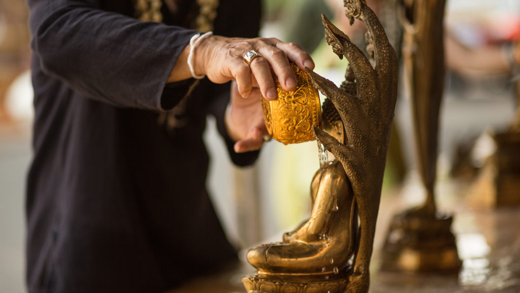 a man pours water over a Buddha statue