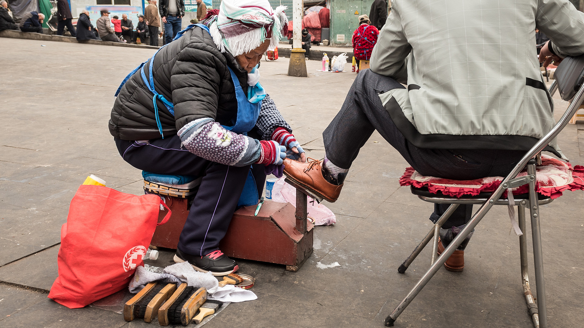 A Miao woman shines shoes on a street in East Asia. 