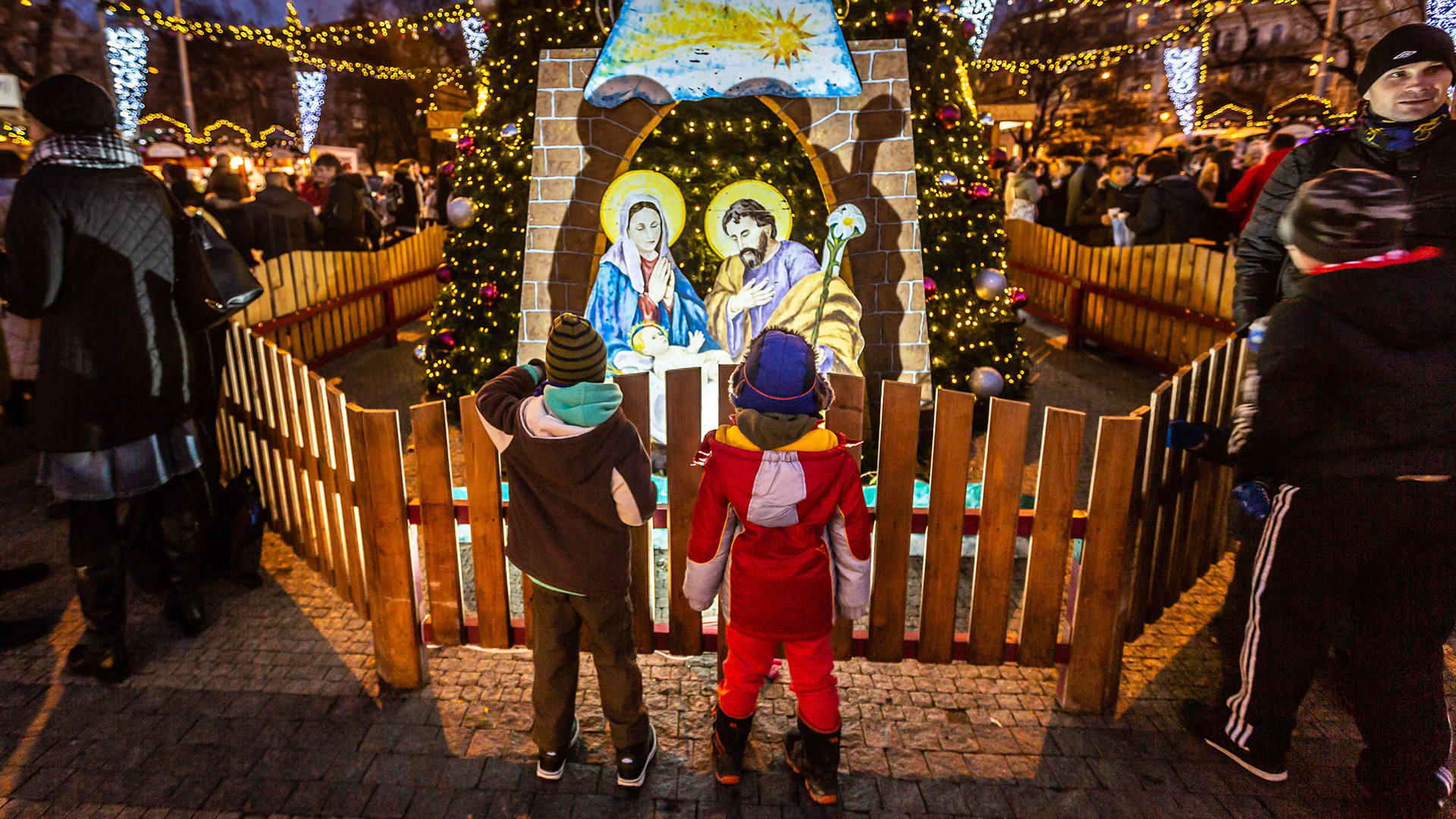 Children at a European Christmas market gaze at a nativity scene. 