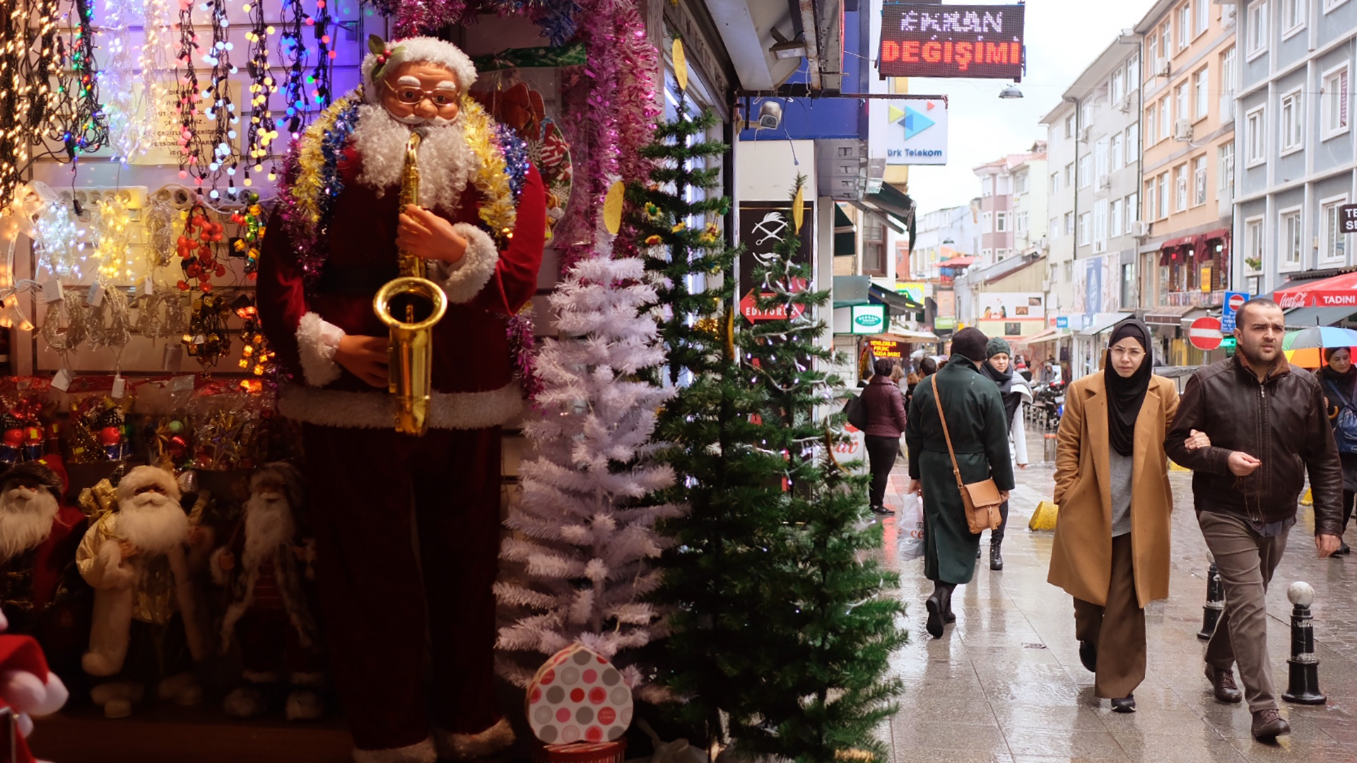 Pedestrians stroll by a storefront in Turkey displaying New Year's decorations.